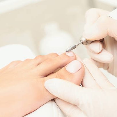 Fußpflege Eine Person erhält eine medizinische Fußpflege oder Pediküre. Eine Hand mit pinken Gummihandschuhen trägt mit einem Pinsel eine türkisfarben
